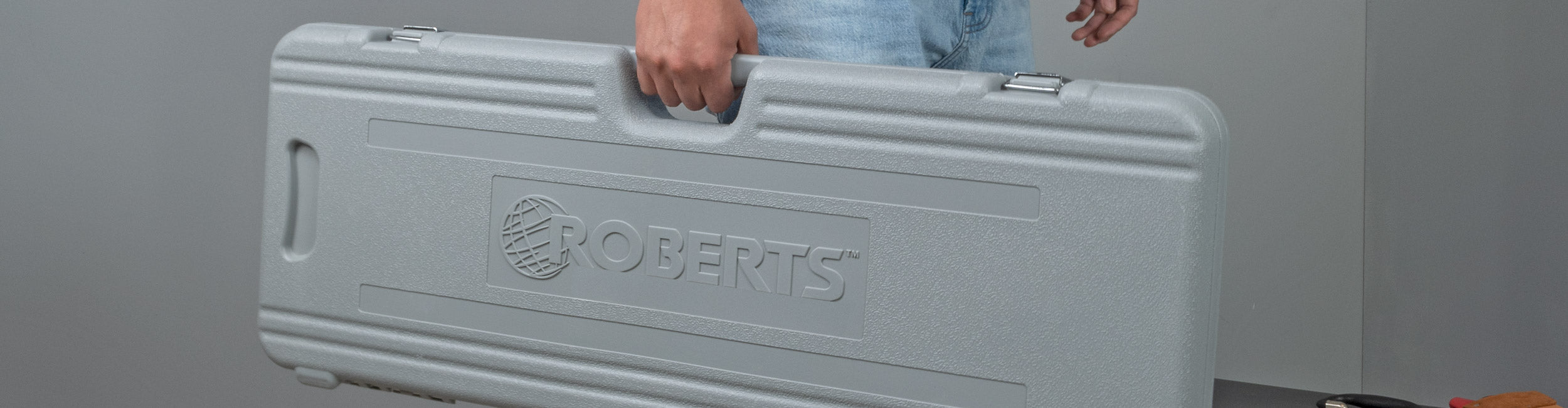 Carpet installer holding a ROBERTS carrying case containing three 3 foot extension tubes for carpet stretchers