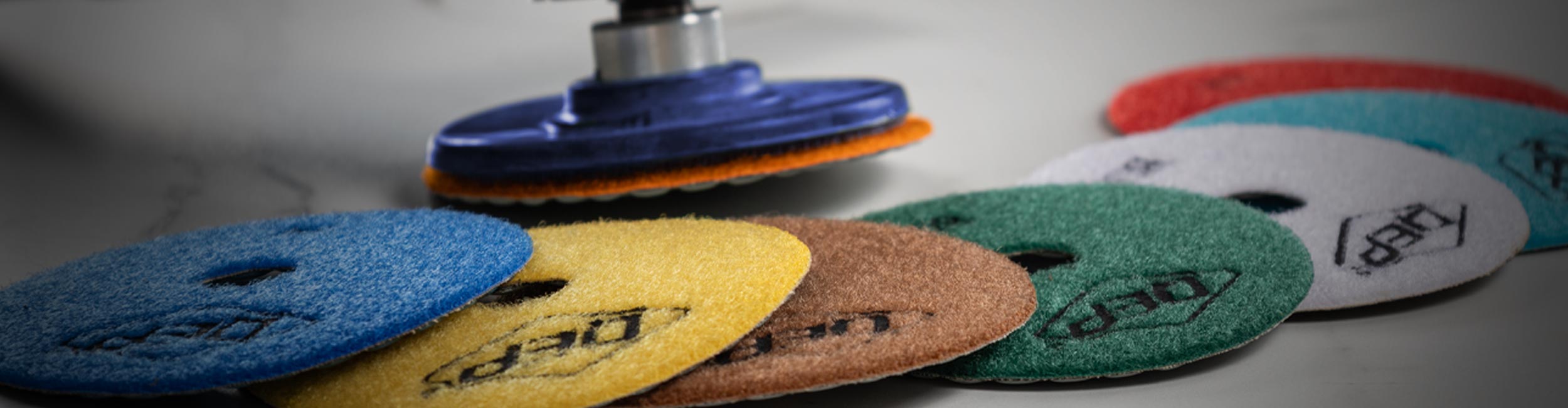 Close-up of QEP's 4" Dry Polishing Pads laid out together with a Backing Pad attached to a grinder