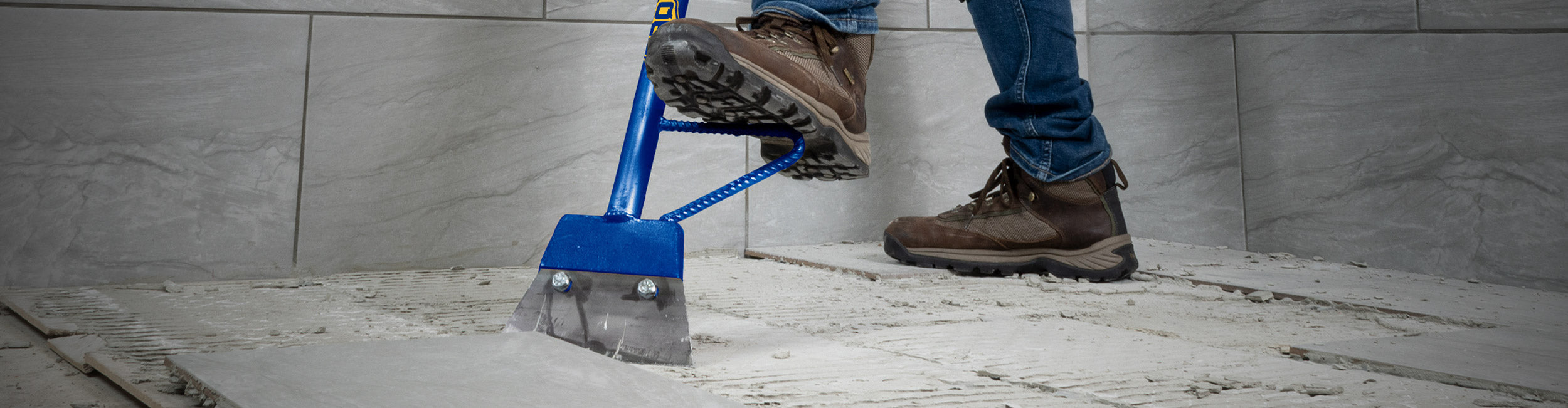 Close-up of a professional installer using a QEP 7" Heavy Duty Floor Scraper to remove old tile and excess debris during demo / tear out