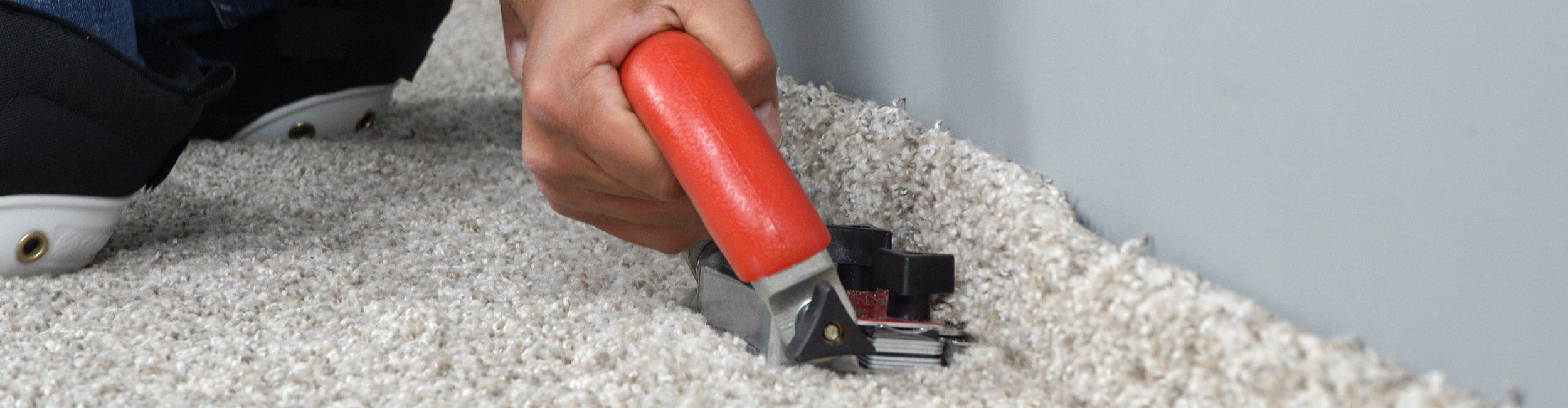 Close-up of an installer using a ROBERTS Conventional Carpet Trimmer to neatly trim carpet along the wall during installation