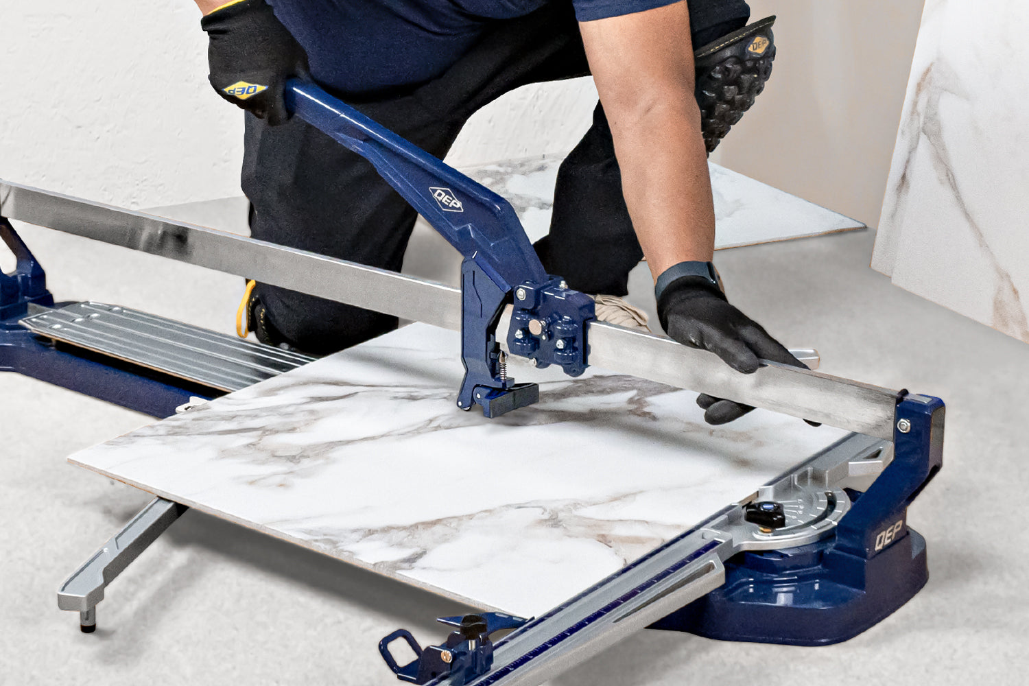 Close-up of a professional installer using QEP's Katana™ SR-41 tile cutter to score a large-format marble-look porcelain tile