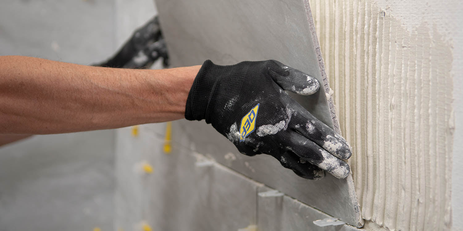Installer placing a large format tile on a wall while using QEP's LASH tile leveling system and SureGrip Tiler's Gloves