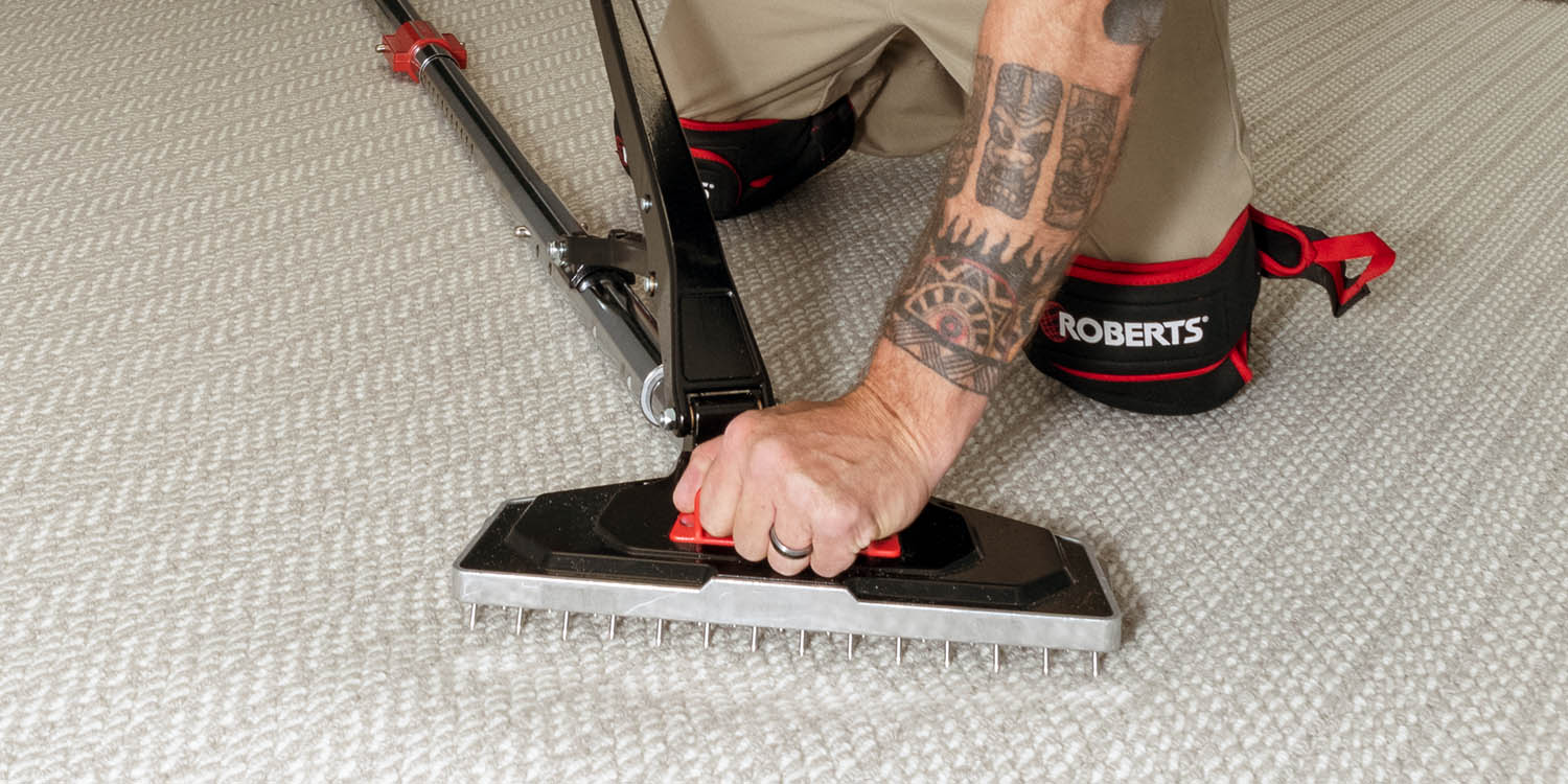 Installer using ROBERTS Falcon Power Stretcher to stretch carpet while wearing ROBERTS knee pads
