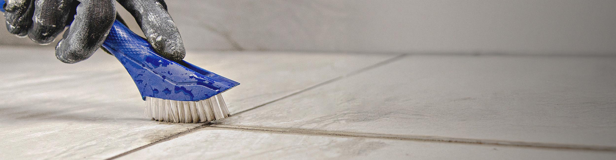 Close-up of installer removing unwanted buildup from grout lines using QEP's Grout Cleaning Brush