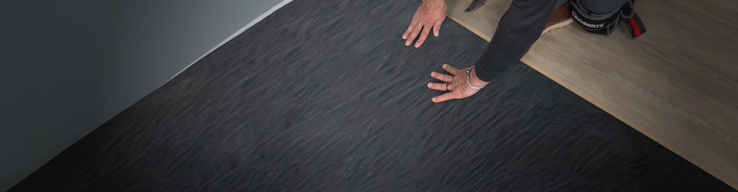 Hands smoothing out ROBERTS Moisture Barricade during vinyl flooring installation