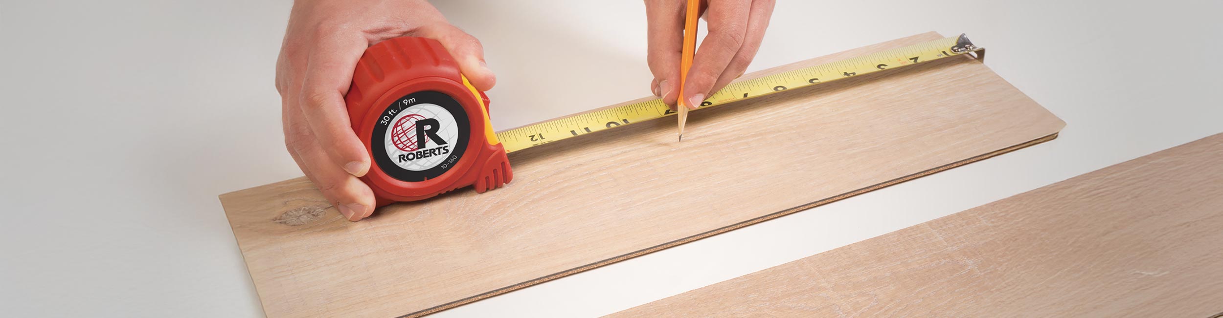 Close-up of installer using ROBERTS 30ft tape measure to get measurements of a flooring plank