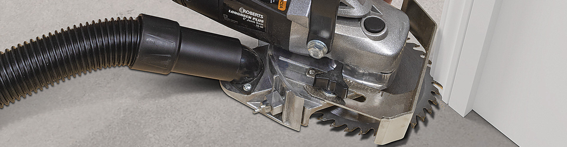 A ROBERTS Longneck Plus 6 inch Jamb Saw in-use undercutting a door jamb with vacuum hose connected to its port