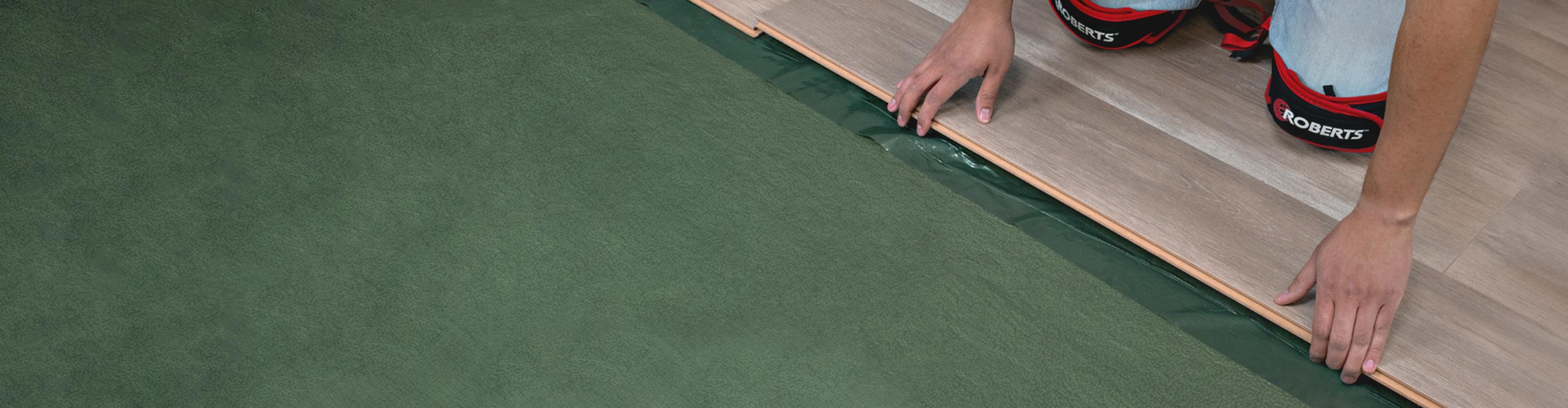 An installer laying engineered wood flooring over ROBERTS First Step Premium Underlayment