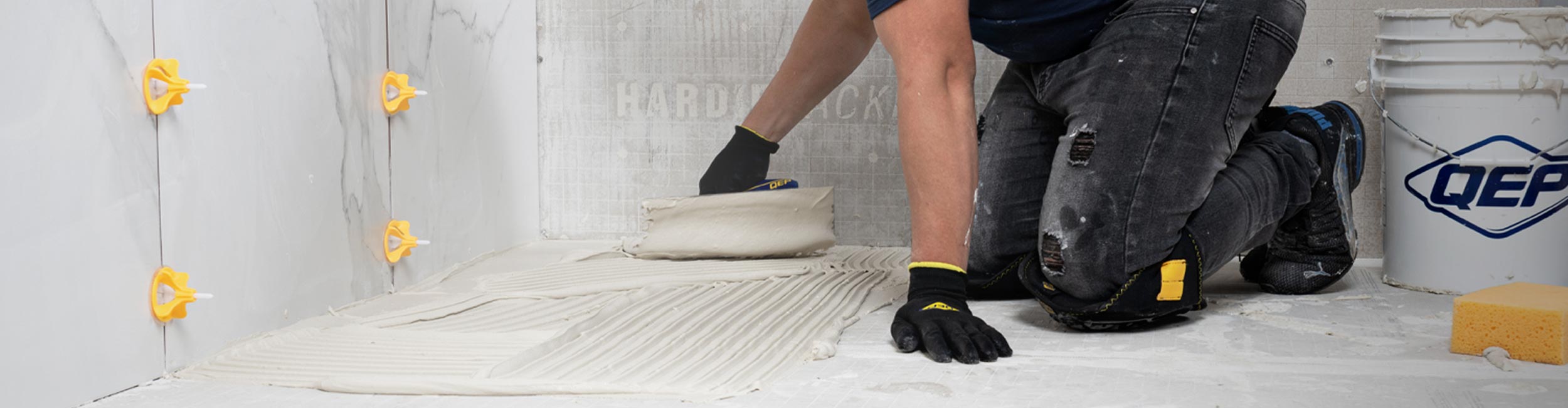 Installer applying thinset with trowel using QEP LASH 360 for alignment and QEP bucket & sponge
