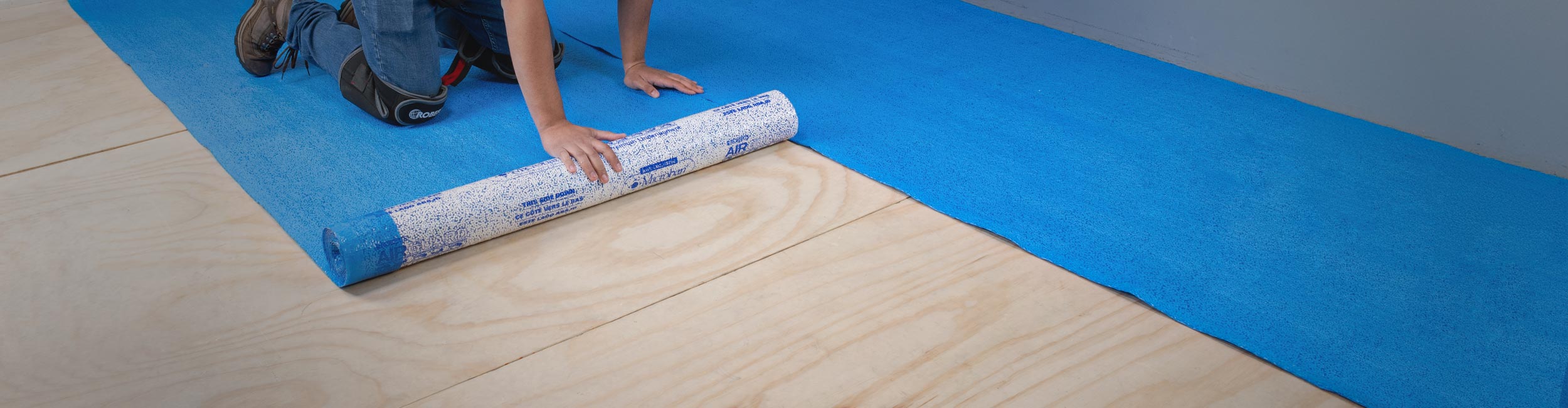 Person rolling out ROBERTS AirGuard Premium Underlayment over plywood subfloor for installation