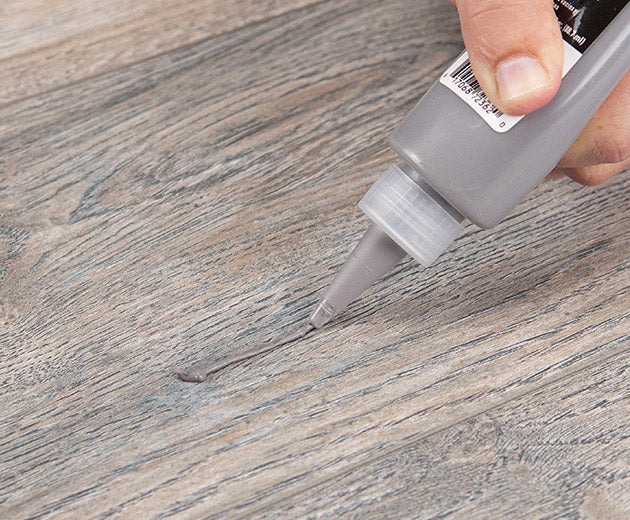 ROBERTS flooring repair putty being applied to a grey wood-look plank floor
