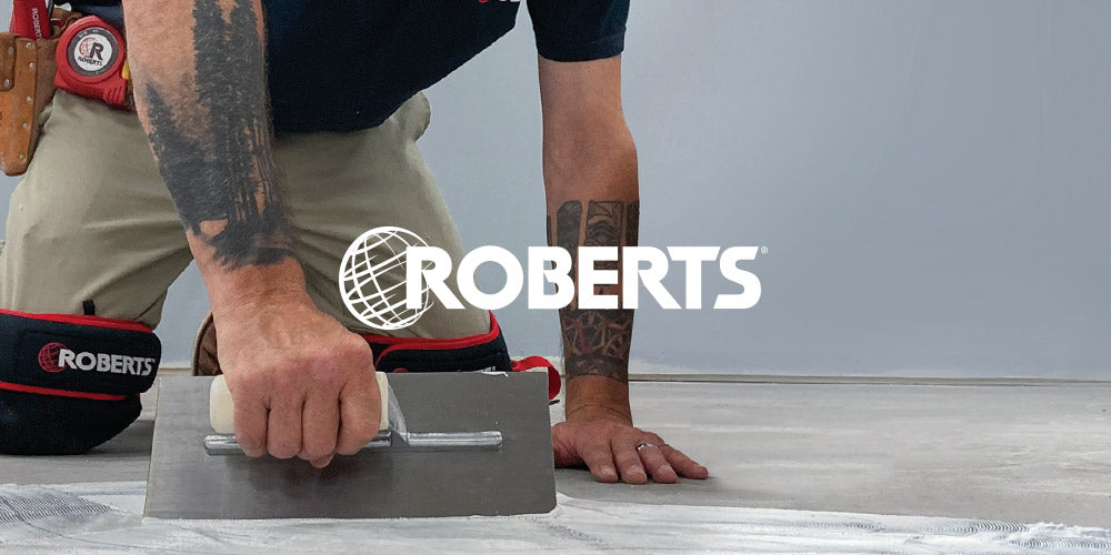 Installer using a ROBERTS wood handle trowel to spread ROBERTS flooring adhesive while wearing ROBERTS knee pads, a ROBERTS Deluxe Grip Pouch containing and ROBERTS carpet knife, and a ROBERTS 30' tape measure on his belt