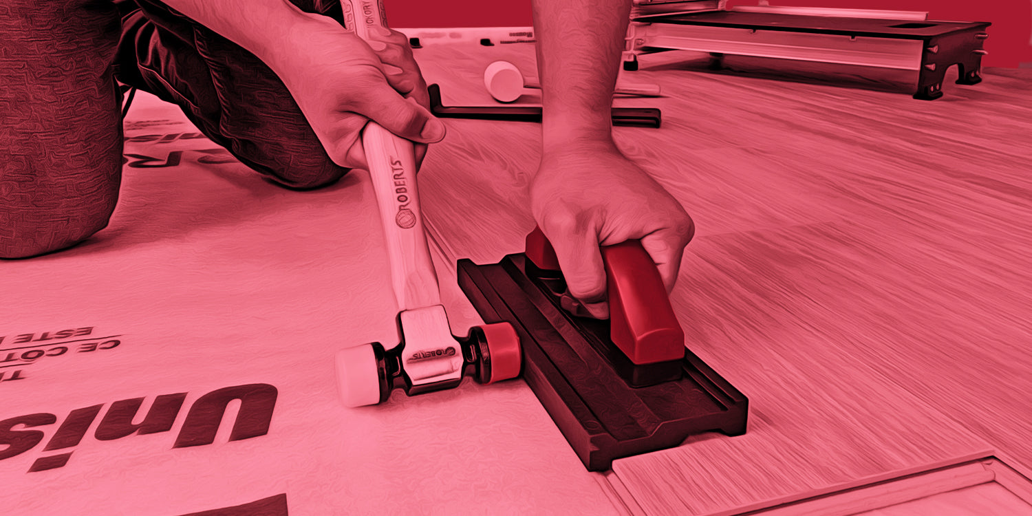 Close-up of an installer using a ROBERTS Double Tap Tapping Block with a dual-headed mallet to fit vinyl planks together during flooring installation