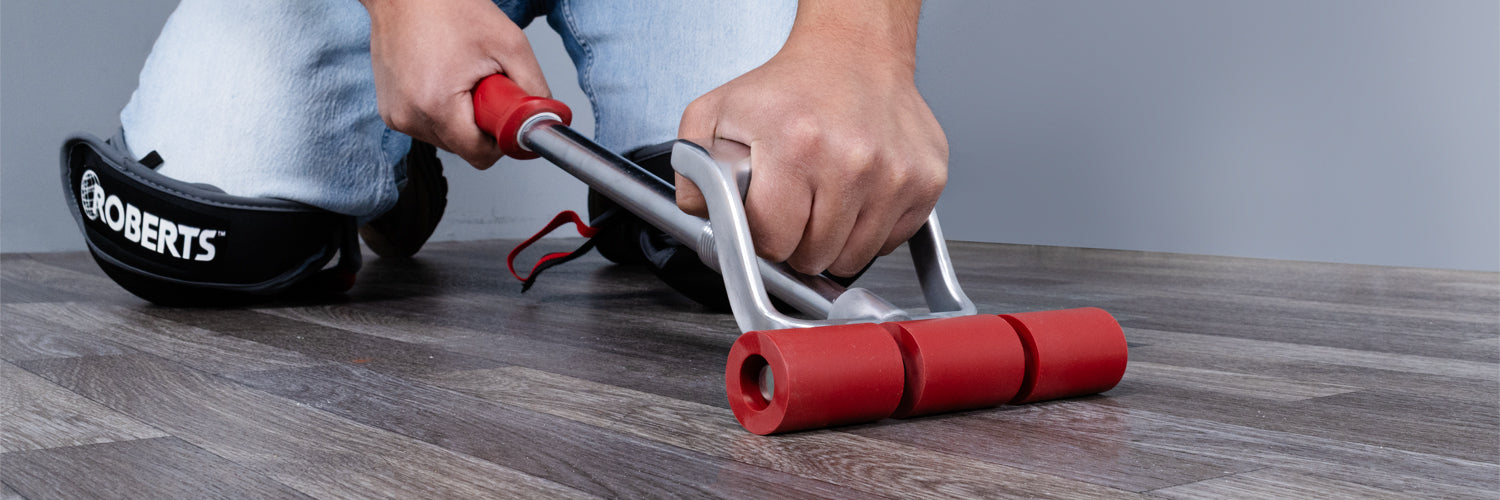 Close-up of a flooring installer using a ROBERTS Power-Lok Floor Roller to press down vinyl or laminate flooring for optimal adhesion
